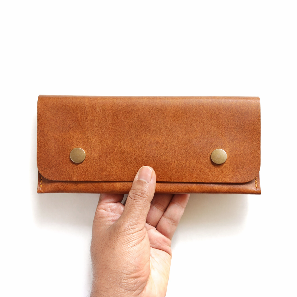 Hand holding a brown leather wallet with gold buttons on a white background