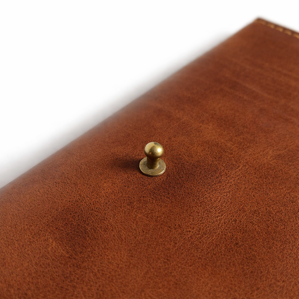 Close-up of a brown leather product with a gold rivet on a white background