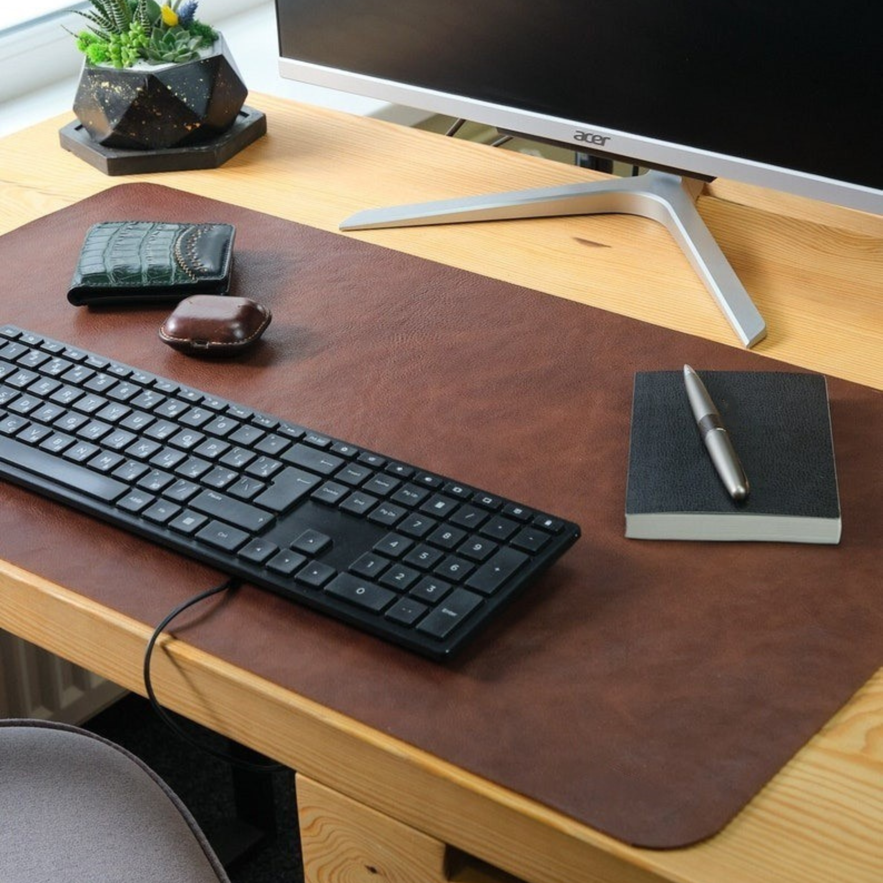 Wooden desk with leather mouse pad, keyboard, notebook, pen, and Acer monitor.