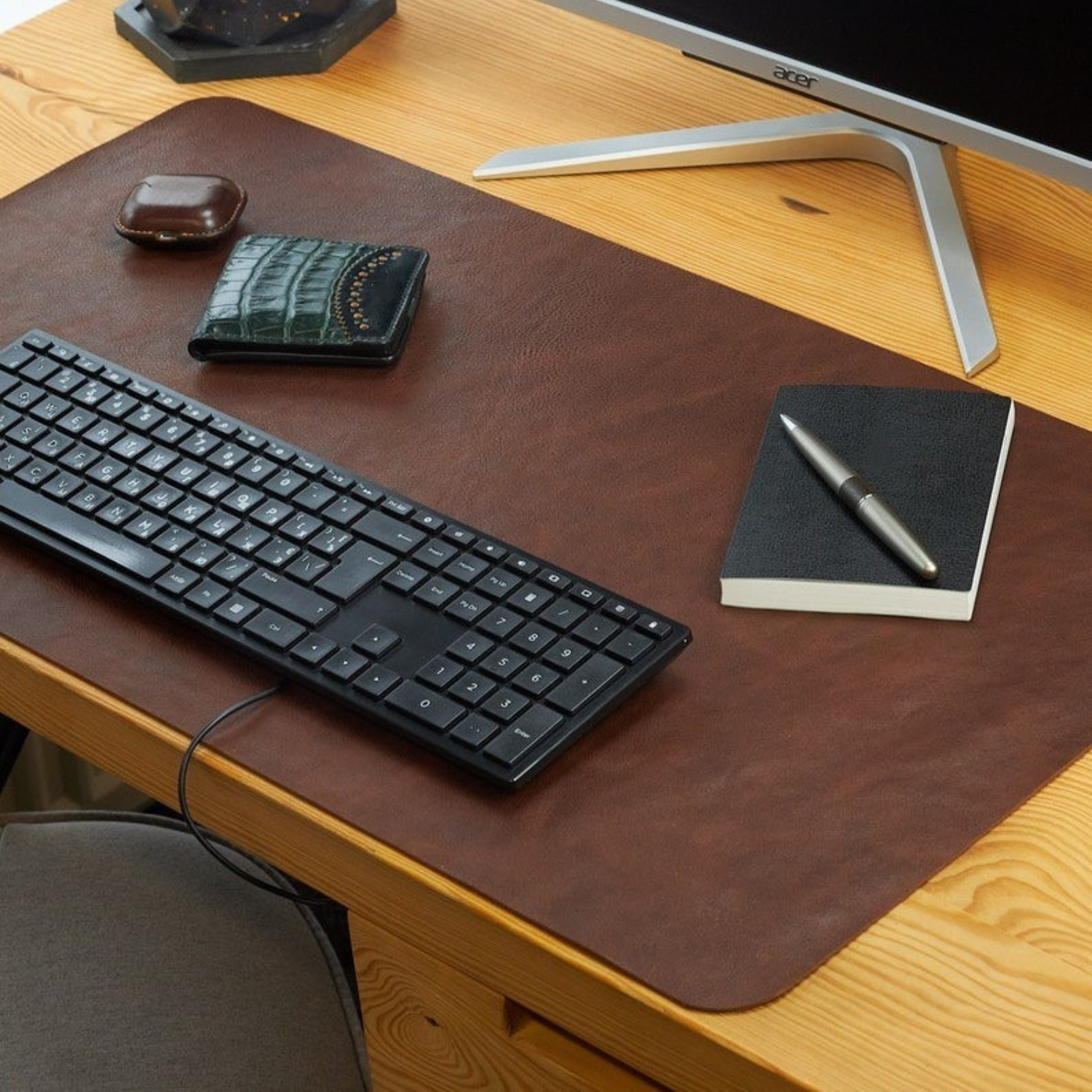 Wooden desk with leather desk pad, keyboard, notebook, pen, and wallet.