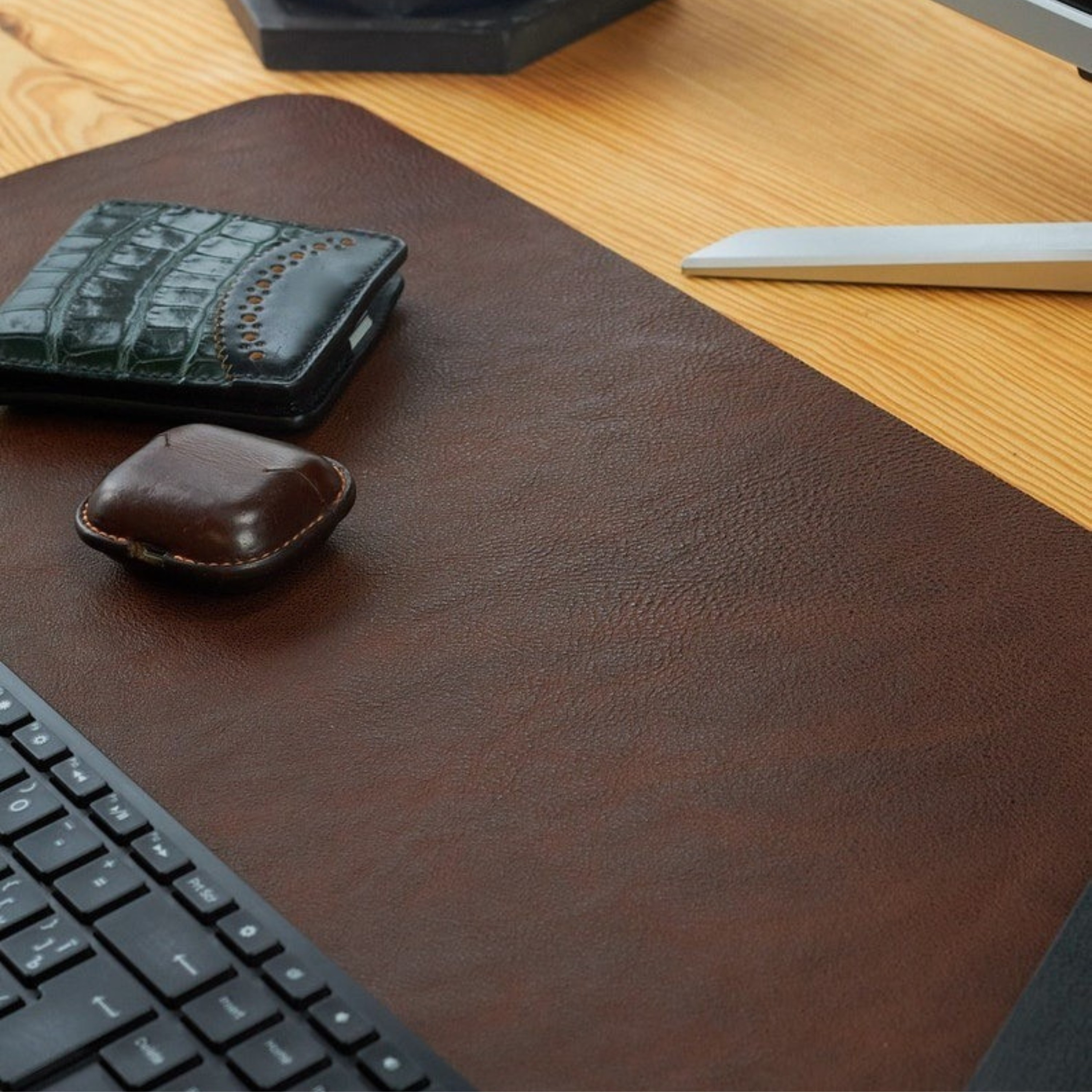 Brown leather desk pad on a wooden desk with a keyboard and wallet.